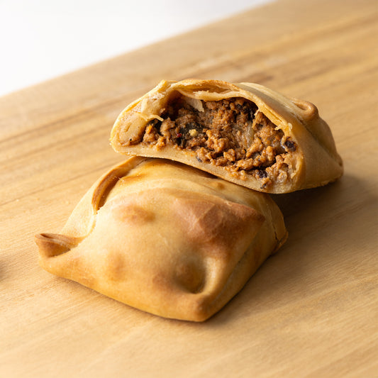 Imagen de empanada chilena de carne molida al horno, con masa dorada y relleno jugoso de carne sazonada, cebolla y especias típicas.

